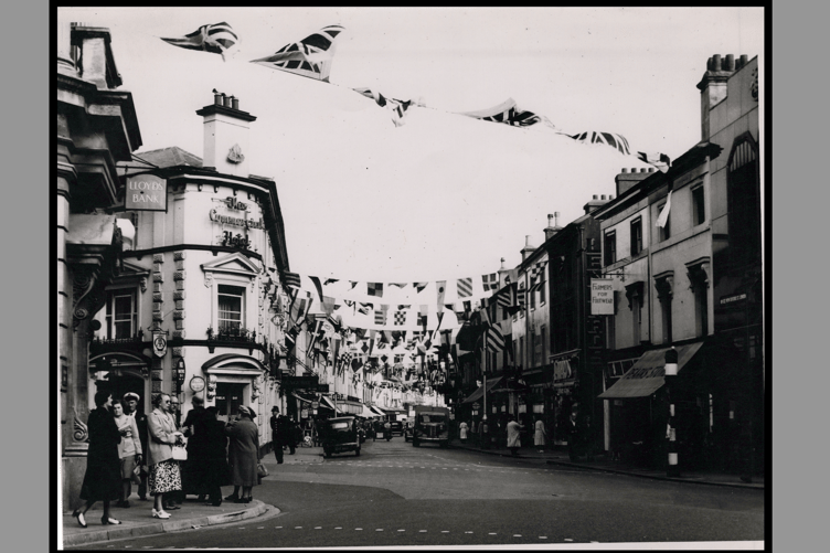 Black and white photograph of Queen Street with Commercial Hotel on left hand side. Street decorated with bunting