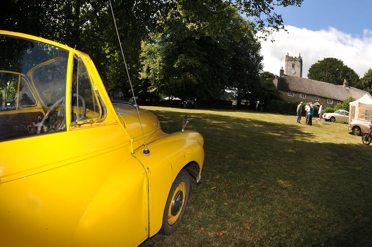 Manaton Show. A bright yellow Morris Minor basks in the summer sun on the Green as part of the classic car show on the day