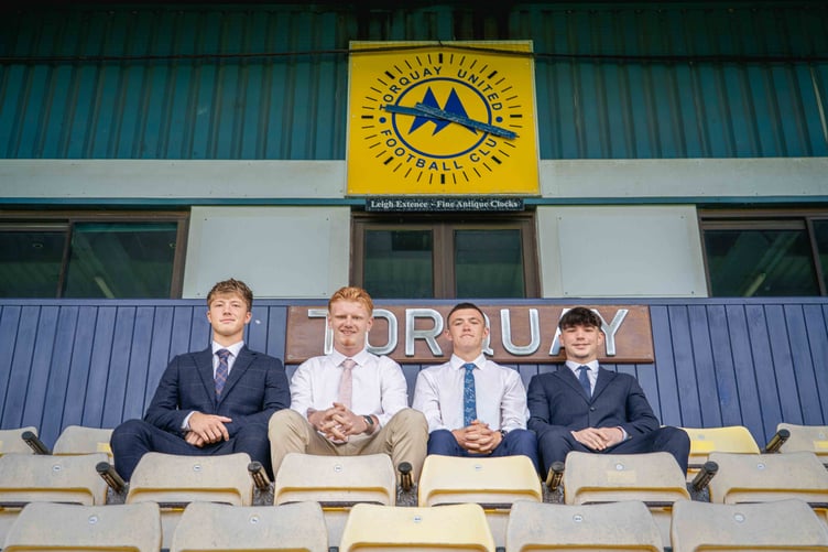 Four posed at Torquay United stand beneath club crest
